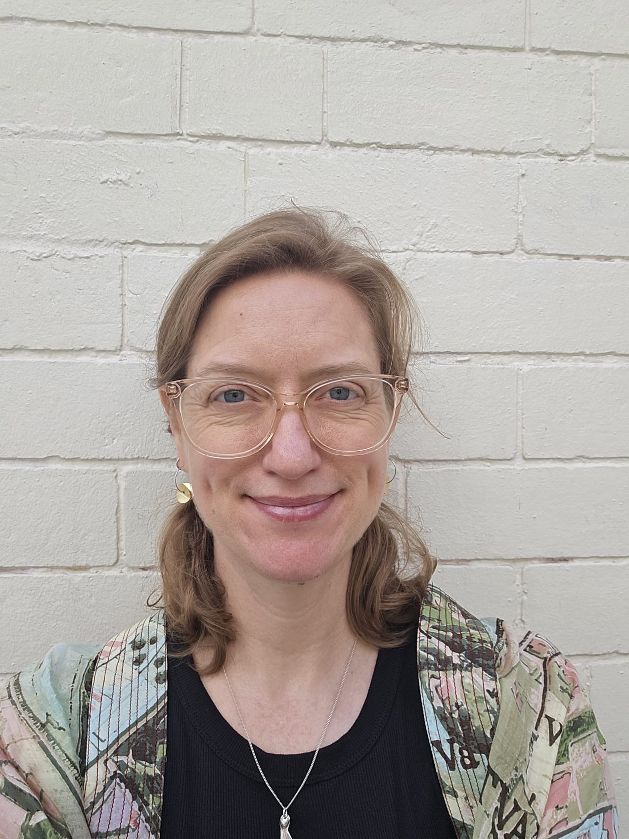 A smiling woman with mid-length dark blonde hair and glasses.