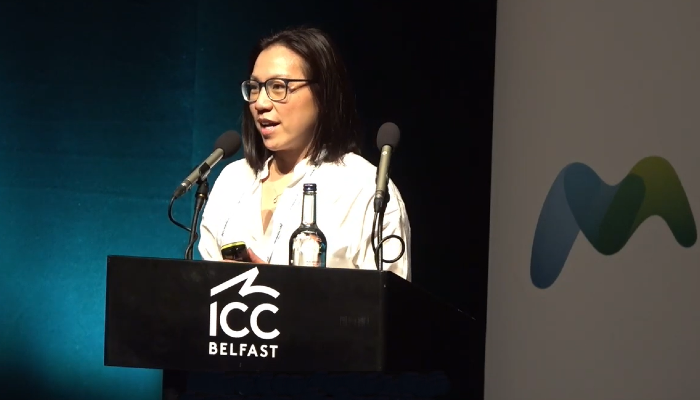 Professor Antonia Ho delivers her 2026 Fleming Prize lecture at the Microbiology Society Annual Conference in Belfast, speaking at a lectern on stage.