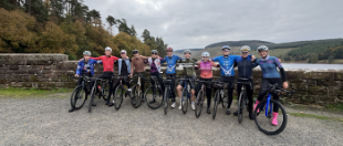 A large group of cyclists pose together with their bikes outdoors, ready to take part in a cycling event.