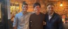 Three smiling men in a pub with a stone wall behind