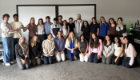 Students and staff from the Business in the Biosciences course pose in two rows in a teaching room. Course leads Dr Anna McGregor, wearing a patterned blue blouse, and Dr Laura McCaughey, wearing a blue scarf, kneel at the centre of the front row.