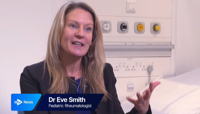 Dr Eve Smith, Sii Paediatric Rheumatologist, speaking and gesturing during an interview with STV News in a hospital setting.