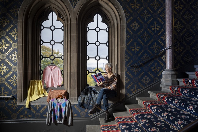 Professor Lynn Abrams. Credit Martin Shields A woman sits on a window ledge reading a book - Knitting in Scotland - with a selction of knitwear on display