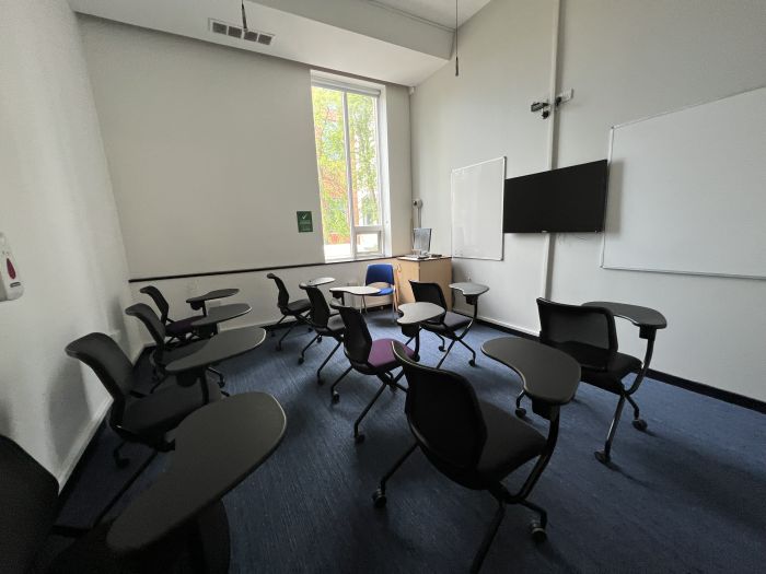 Flat floored teaching room with tablet chairs, whiteboards, video monitor, PC, and lecturer's chair.