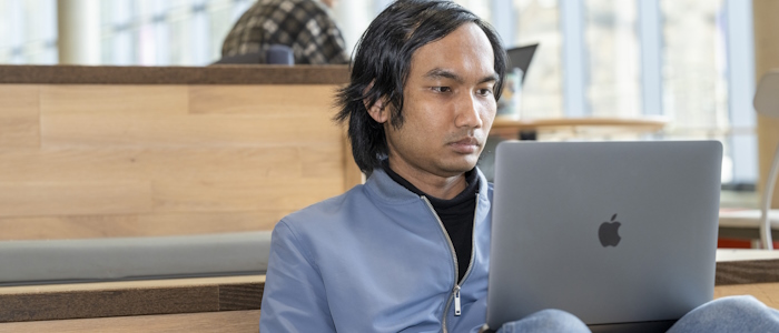 a student sitting using a laptop in the JMS building