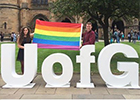Students holding a rainbow flag by the big UofG letters