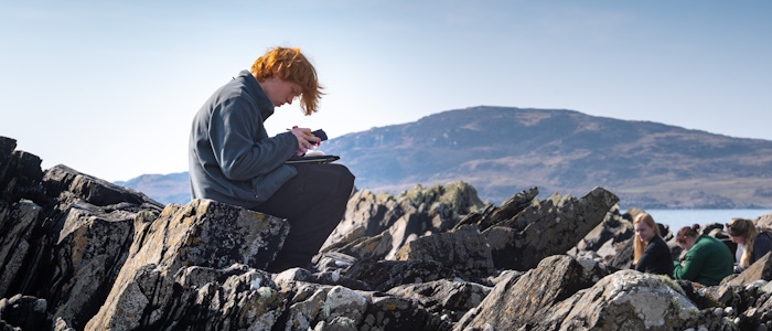 Geographical & Earth Sciences student taking notes on rocks by a beach