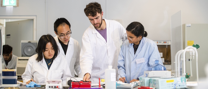 a lecturer and students gathered around a desk in a lab