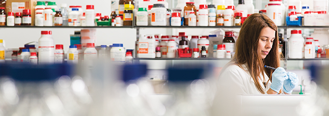 Student in lab - backround shelves with colourful bottles and jars