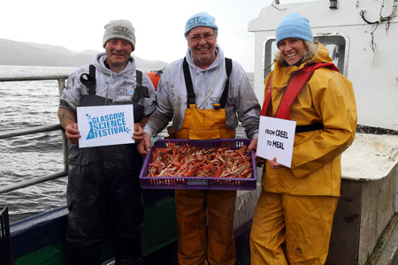 Photograph showing GSF director Dr Deborah McNeill with 2 fisherman. They are holding a tray of shellfish with signs saying Glasgow Science Festival and From Creel to Meal. 
