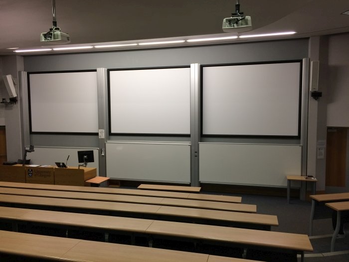 Raked lecture theatre with fixed seating, projectors, screens, whiteboards and PC