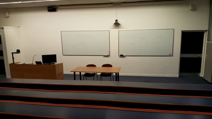 Raked lecture theatre with fixed seating, projectors, screens, visualisers, and PC