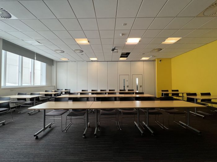 Flat floored teaching room with rows of tables and chairs, and projector.