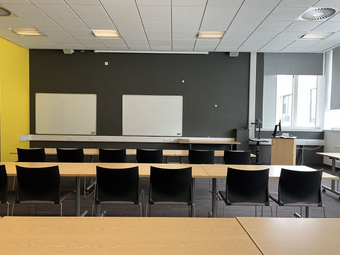 Flat floored teaching room with rows of tables and chairs, whiteboards, visualiser, and PC.