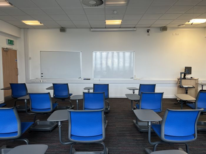 Flat floored teaching room with tablet chairs, whiteboards, visualiser, and PC.