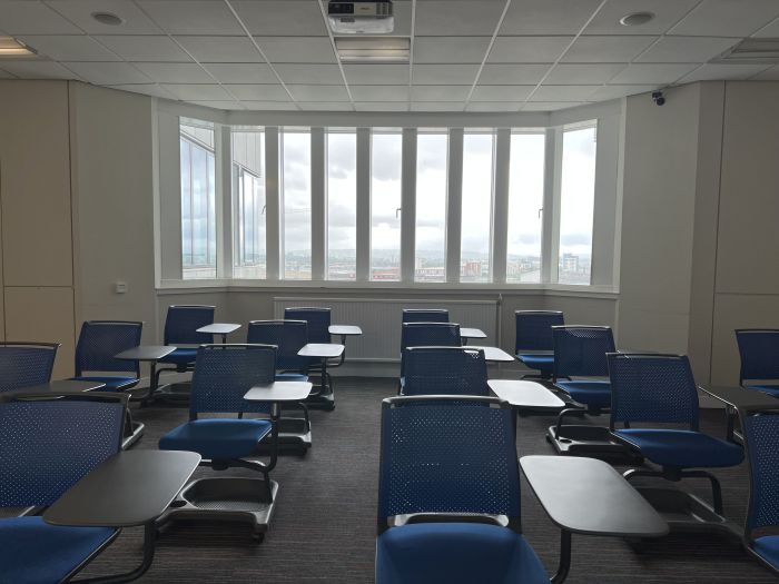 Flat floored teaching room with tablet chairs and projector.