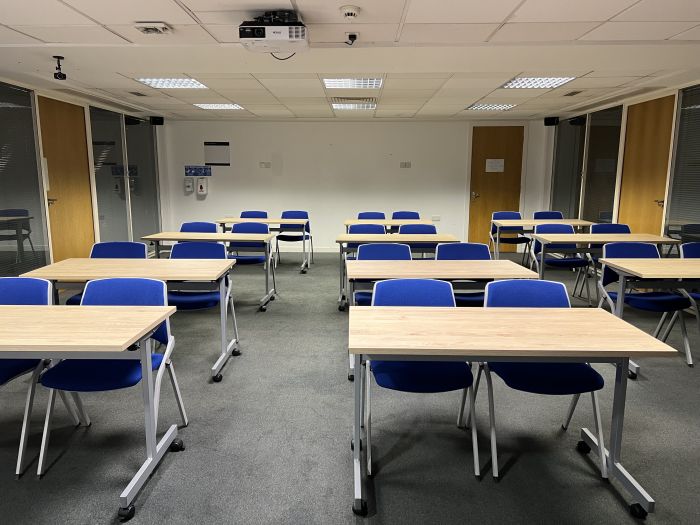 Flat floored teaching room with rows of tables and chairs, and projector.