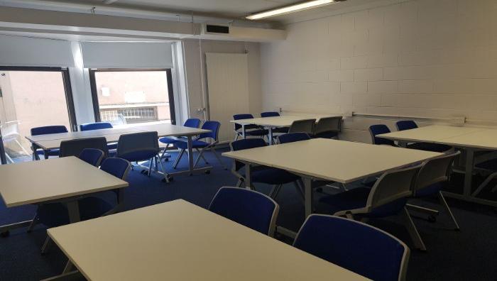 Flat floored teaching room with tables and chairs in groups.