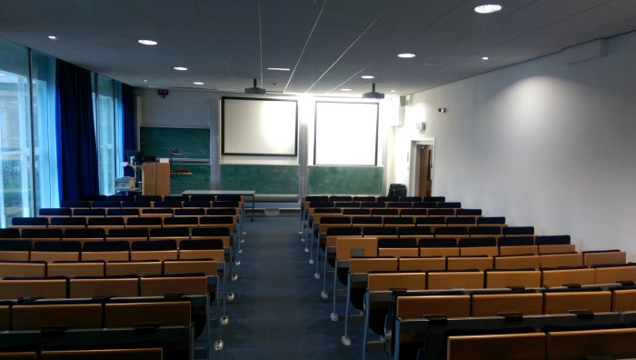 Raked lecture theatre with fixed seating, projectors, screens, and chalkboards