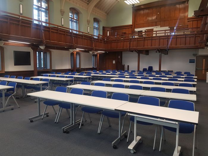 Flat floored hall with rows of tables and chairs, and projectors..