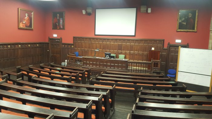 Raked lecture theatre with fixed seating, screen, and whiteboard