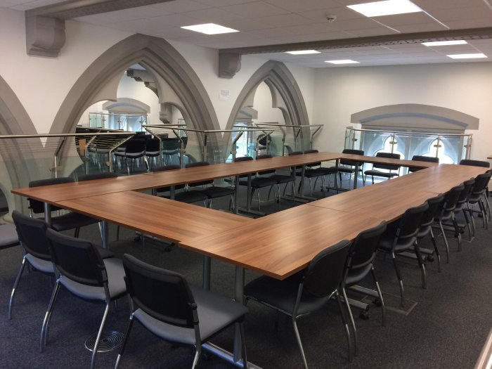 Flat floored teaching room with tables and chairs in round table set-up in back of room