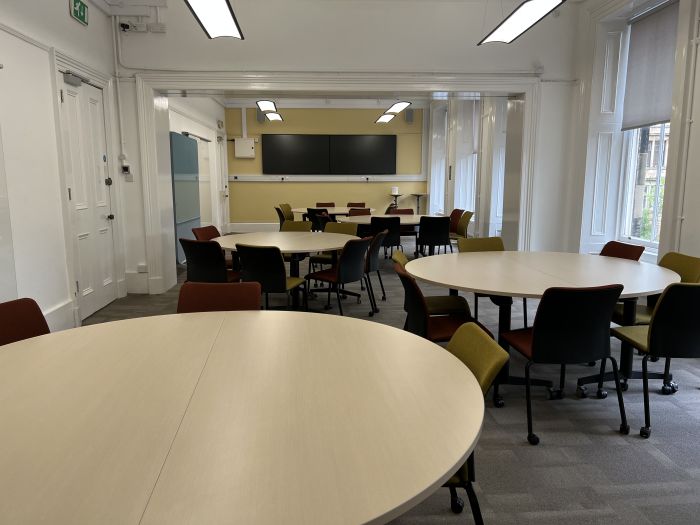 Flat floored teaching room with tables and chairs in groups, video monitor, and moveable glassboard.