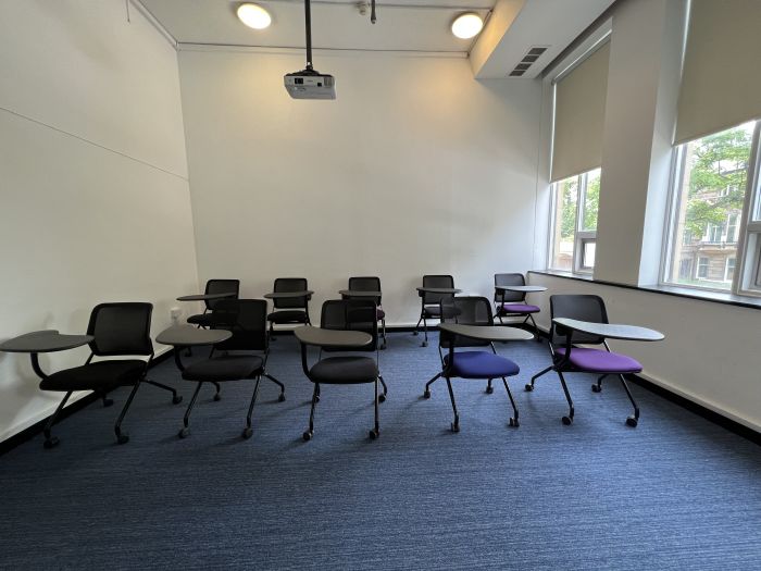 Flat floored teaching room with tablet chairs and projector.