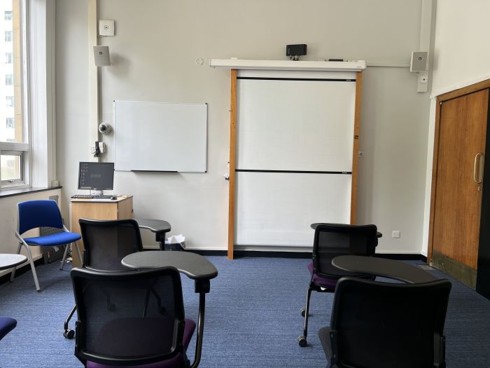 Flat floored teaching room with tablet chairs, whiteboards, PC, and lecturer's chair.