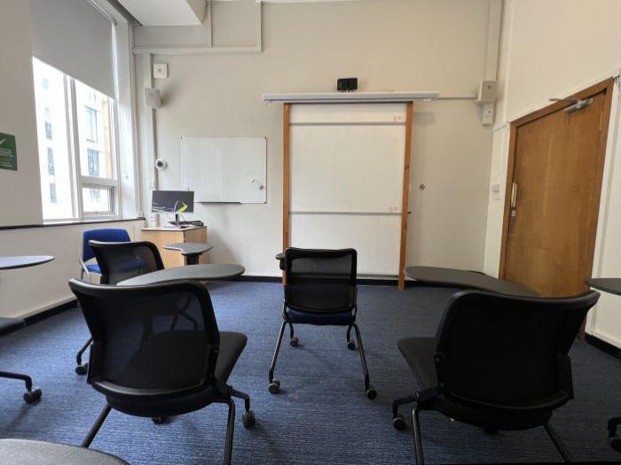 Flat floored teaching room with tablet chairs, whiteboards, PC, and lecturer's chair.