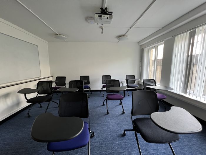 Flat floored teaching room with tablet chairs, whiteboard, and projector.