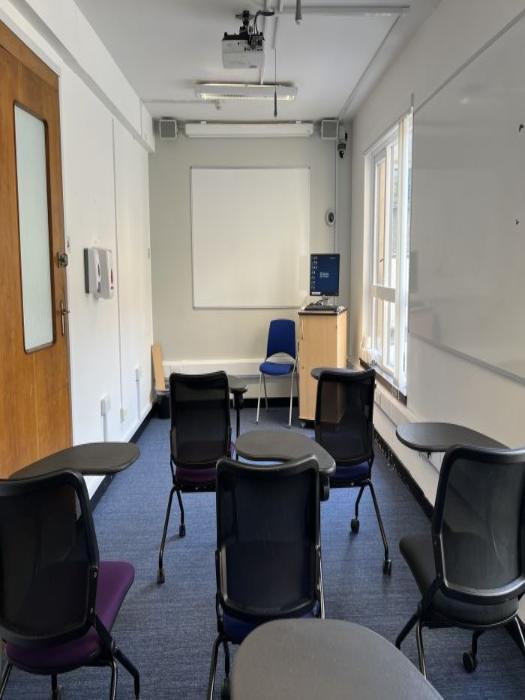 Flat floored teaching room with tablet chairs, whiteboard, projector, PC and lecturer's chair.