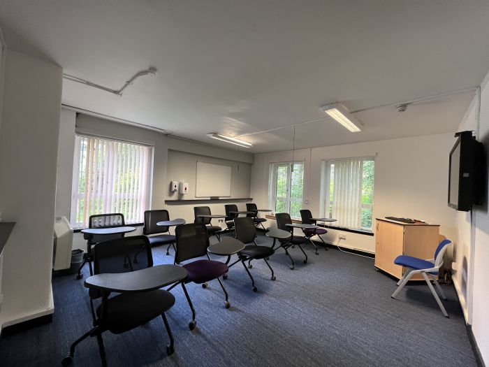 Flat floored teaching room with tables and chairs in round table set-up and whiteboard