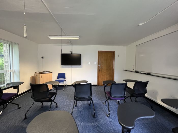 Flat floored teaching room with tables and chairs in round table set-up and video monitor