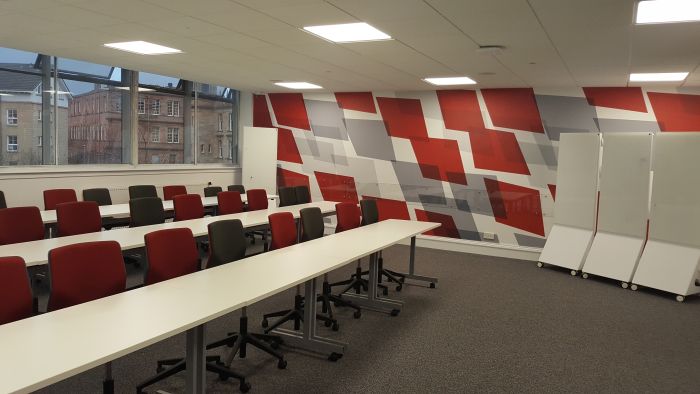 Flat floored teaching room with rows of tables and chairs, and movable whiteboards.