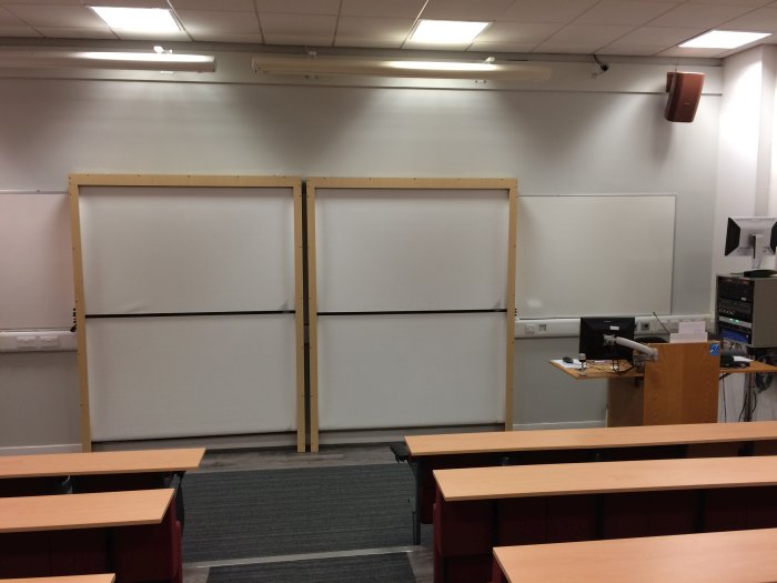 Raked lecture theatre with fixed seating, whiteboards, and PC