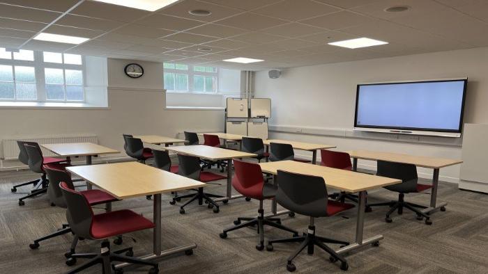 Flat floored teaching room with rows of tables and chairs, smart screen, handheld whiteboards, and moveable whiteboard.