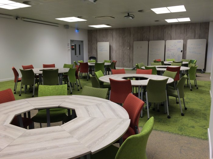 Flat floored teaching room with groups of round tables and chairs and movable glassboards