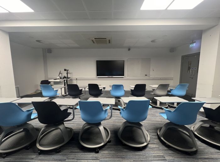 Flat floored teaching room with rows of tablet chairs, smart screen, whiteboard, visualiser, and PC