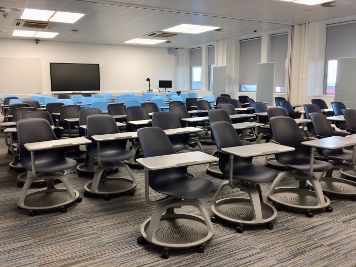Flat floored teaching room with rows of tablet chairs and smart screen