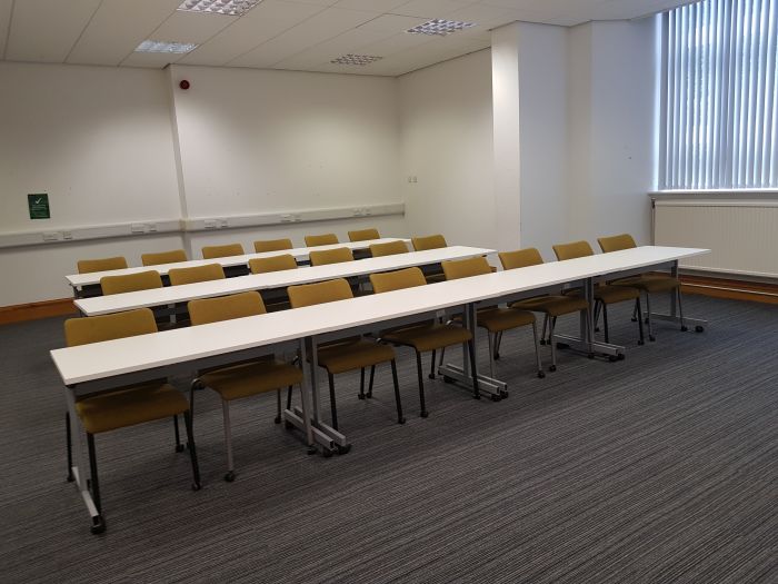 Flat floored teaching room with rows of tables and chairs.