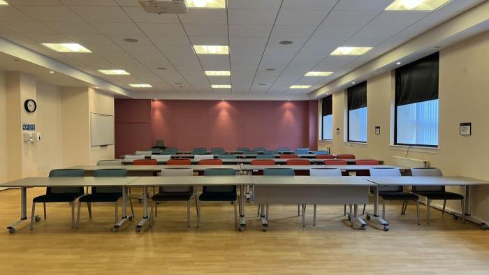 Flat floored teaching room with rows of tables and chairs, whiteboard, and projector.