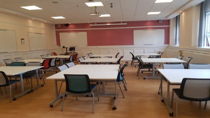 Flat floored teaching room with groups of tables and chairs, whiteboards, PC, visualiser, and projector.