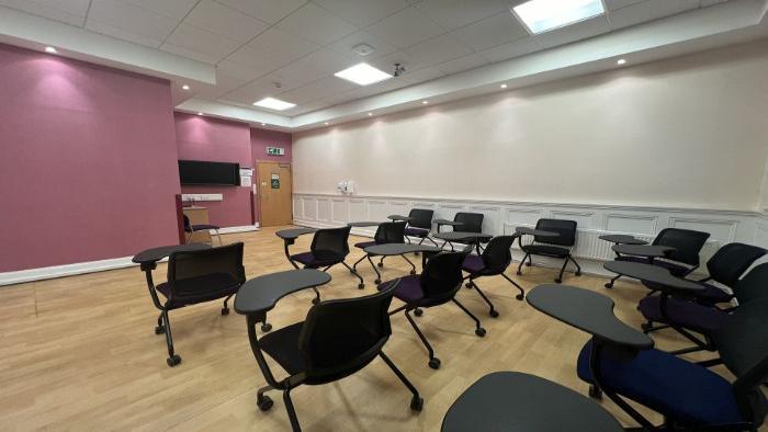 Flat floored teaching room with rows of tablet chairs, lecturer's chair, and video monitor.