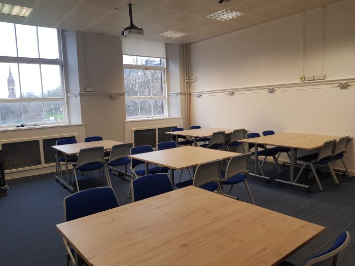 Flat floored teaching room with tables and chairs in groups, and projector.