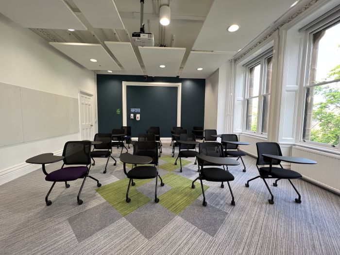 Flat floored teaching room with tablet chairs and projector.