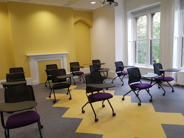 Flat floored teaching room with tablet chairs and projector.