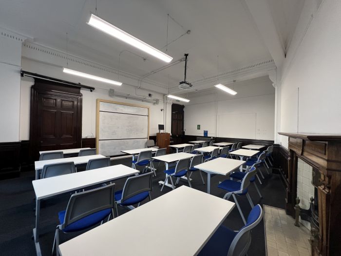 Flat floored teaching room with rows of tables and chairs, whiteboard, projector, and PC.