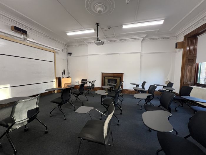 Flat floored teaching room with rows of tablet chairs, whiteboard, projector, lectern, and PC.