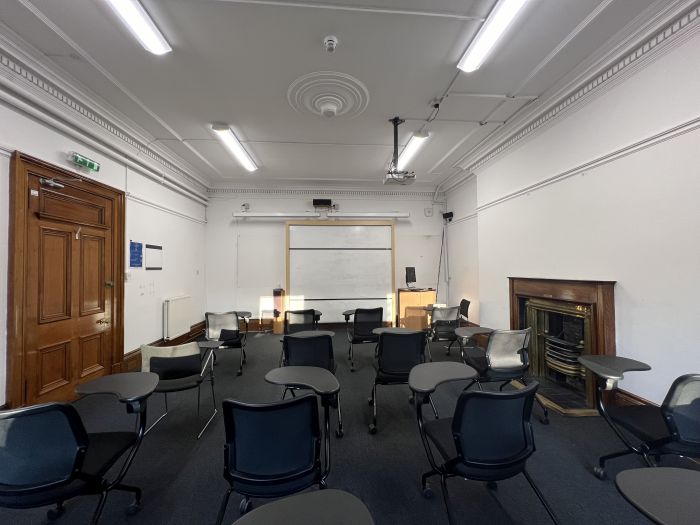 Flat floored teaching room with rows of tables and chairs, whiteboards, screens, and PC